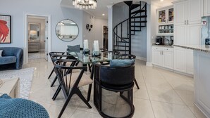 Eine moderne Küche mit weißen Schränken, einer schwarzen Wendeltreppe und einem Essbereich mit einem Glastisch und schwarzen Stühlen.