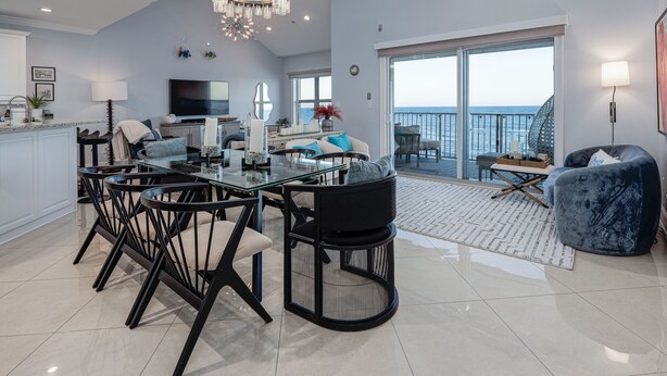 Ein großzügiger Wohnbereich mit Esstisch, Stühlen, einer Couch und einem Balkon mit Meerblick.
