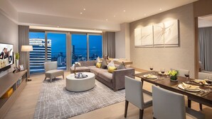 A modern living room with a sofa, coffee table, dining table set for four, and a city view through large windows.