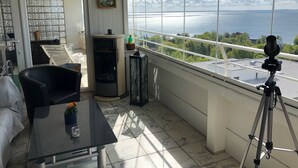 A balcony with a telescope, a table with a flower, and a view of the sea.