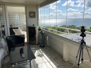 Ein Balkon mit einem Teleskop, einem Tisch mit einer Blume und Blick aufs Meer.