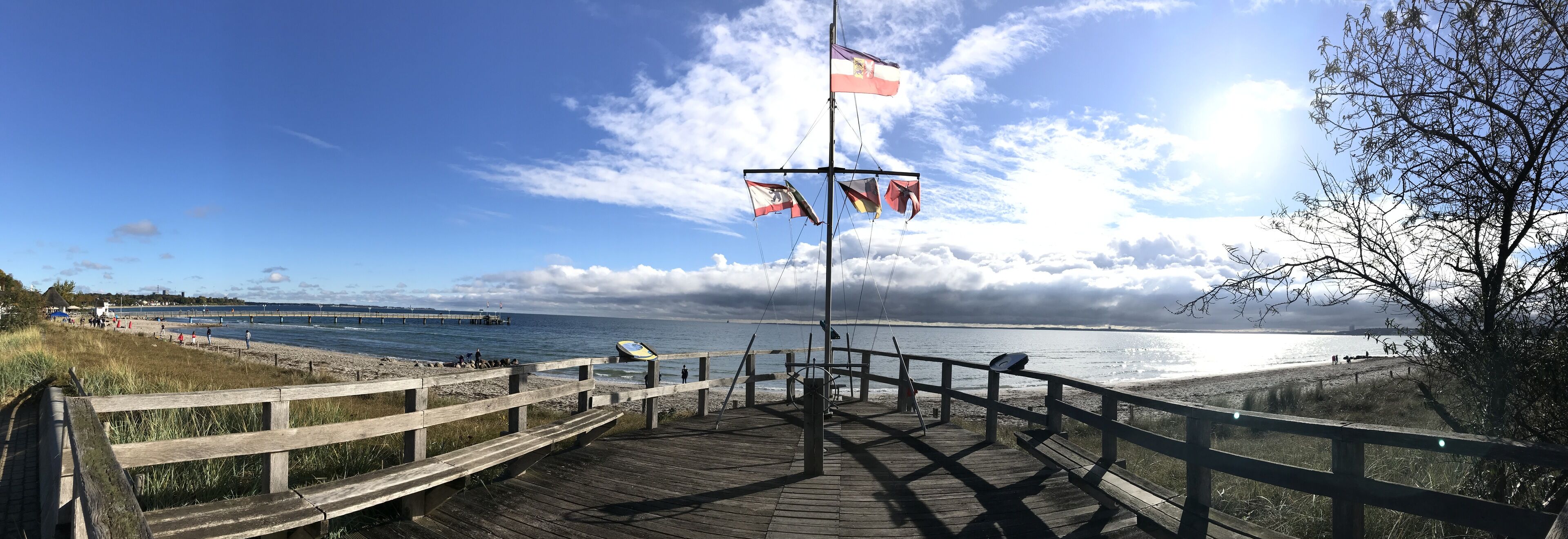 Un muelle de madera que conduce a una playa, con un espigón al fondo.