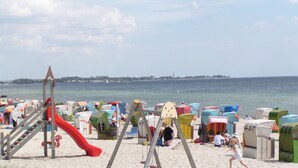 A beach with colorful beach huts, a red slide, and a swing set.