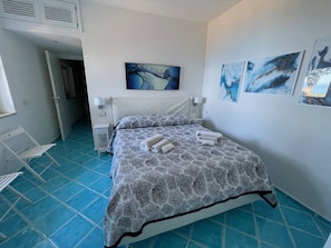 Un dormitorio con cama, mesita de noche, un cuadro colgado en la pared y piso de baldosas azules.