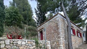 A stone building with red shutters, a stone wall, and a red chair.