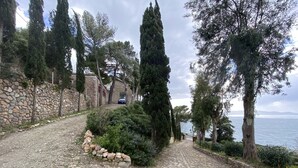 A cobblestone path leading to a stone wall with a car parked in the background.