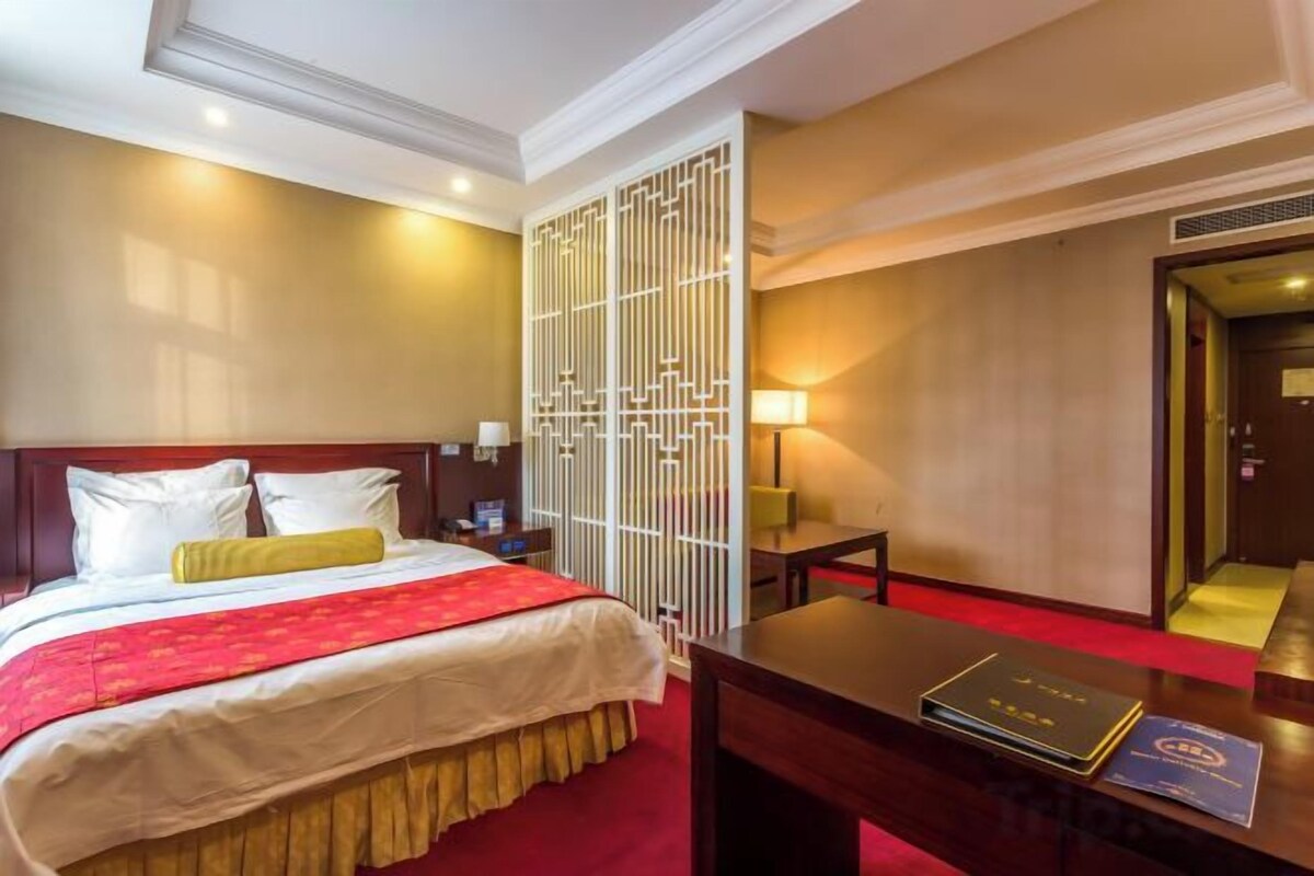 A hotel room with a bed, a desk, a chair, and a mirror.