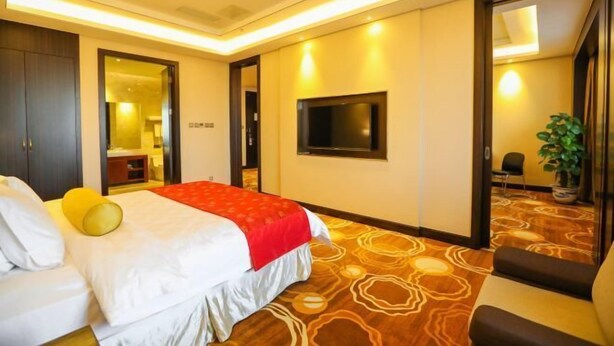 A hotel room with a bed, a TV, a mirror, and a plant. - Yangfang Shengli Hotel (Beijing)