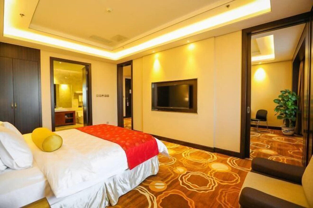 Una habitación de hotel con una cama, televisión, espejo y planta.