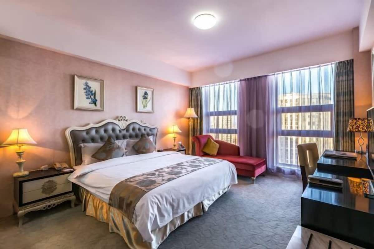 A hotel room with a large bed, bedside tables, a desk, and a red sofa.