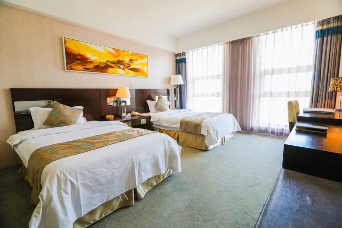 Habitación de hotel con dos camas, un escritorio, una silla, una lámpara y un cuadro en la pared.