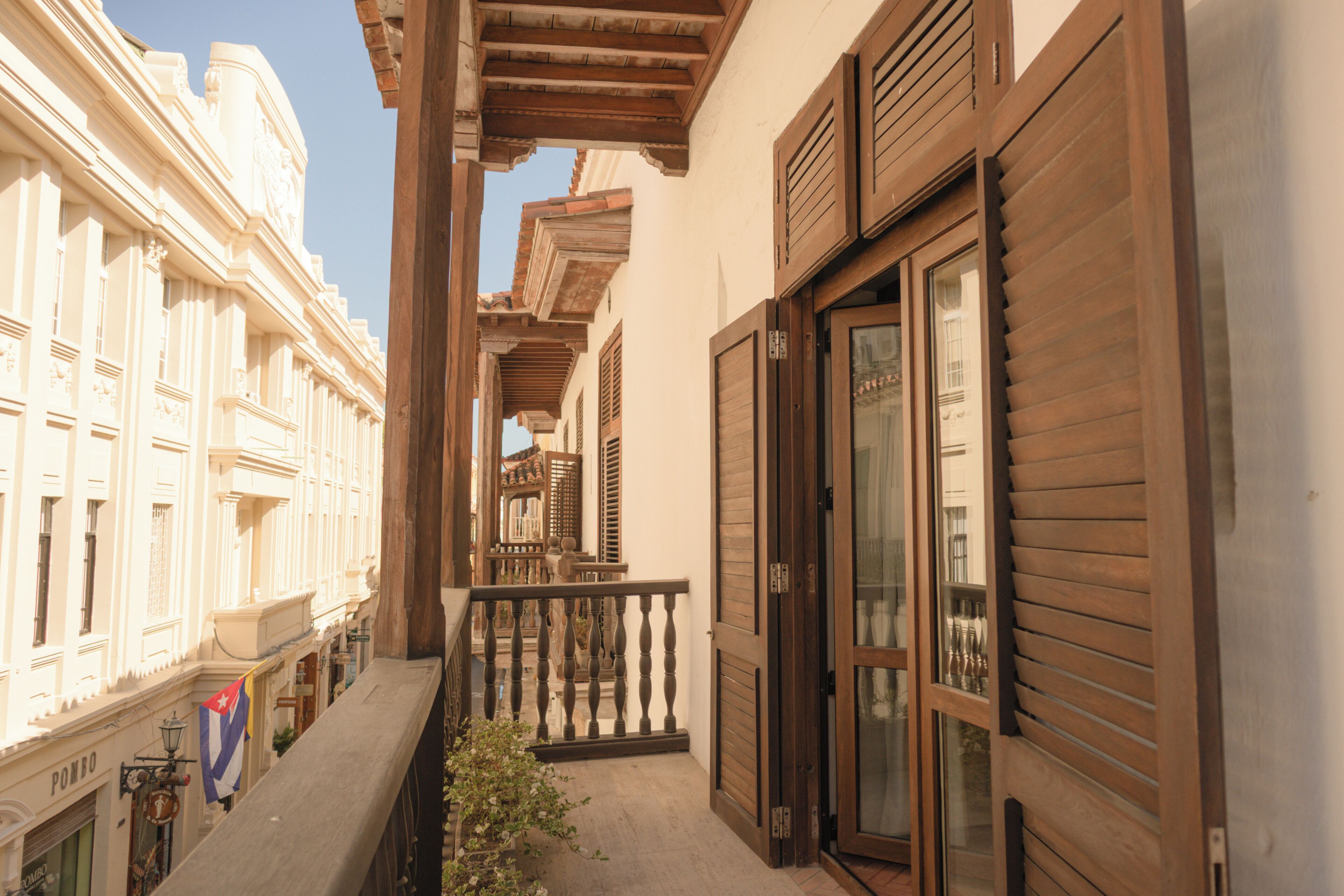 A narrow alleyway with buildings on either side, wooden shutters, and a balcony with a railing.
