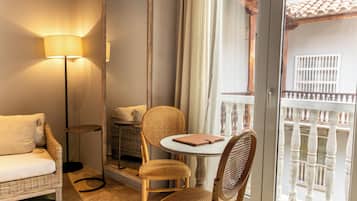 A room with a wicker sofa, a round table with a notebook, a floor lamp, and a balcony with a railing.