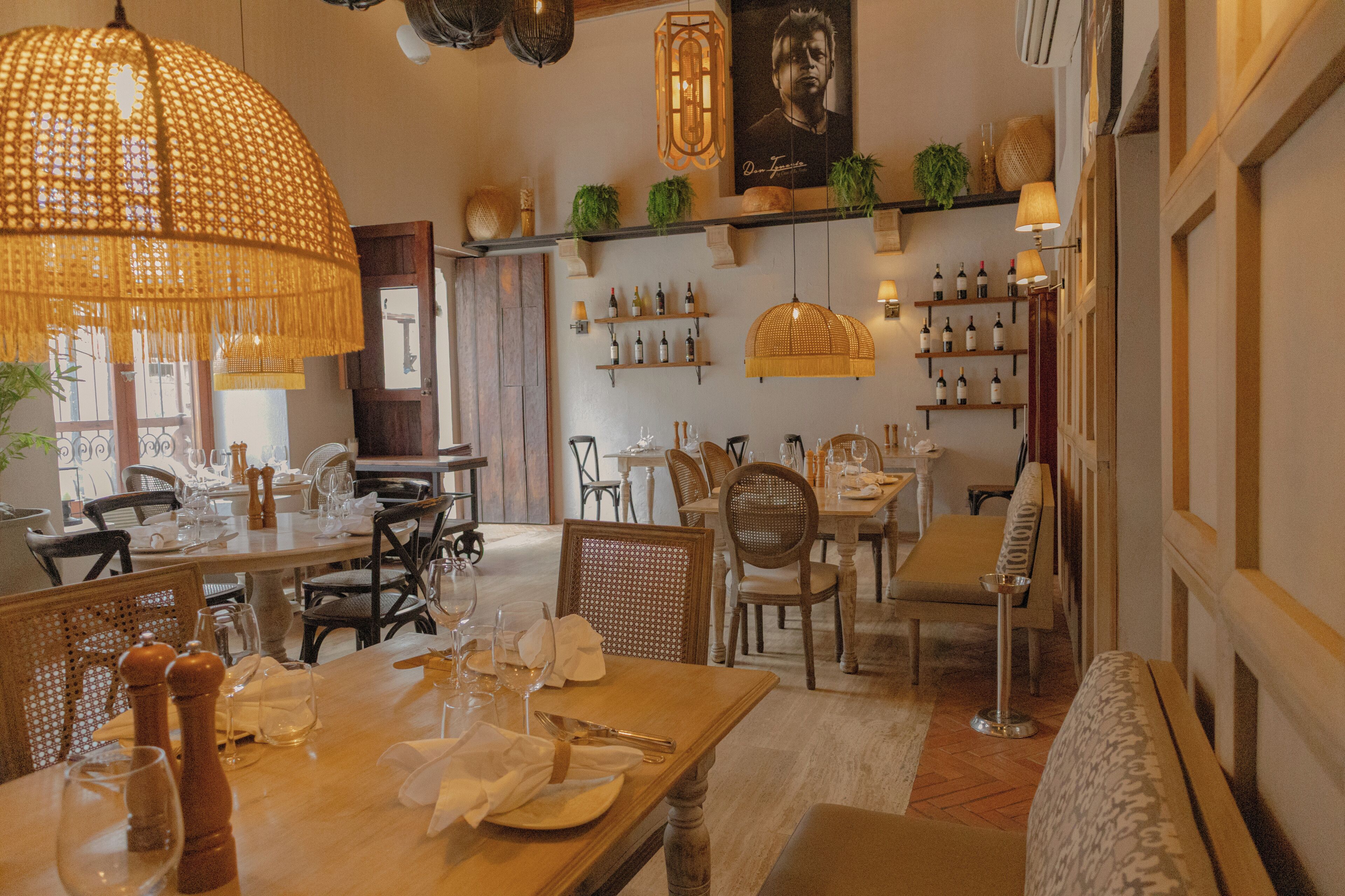 A restaurant with wooden tables, wicker chairs, and hanging wicker lamps.