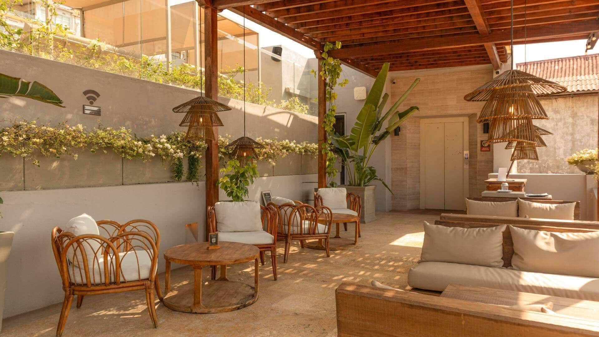 An outdoor patio with wicker furniture, a wooden ceiling, and a wall with climbing plants.