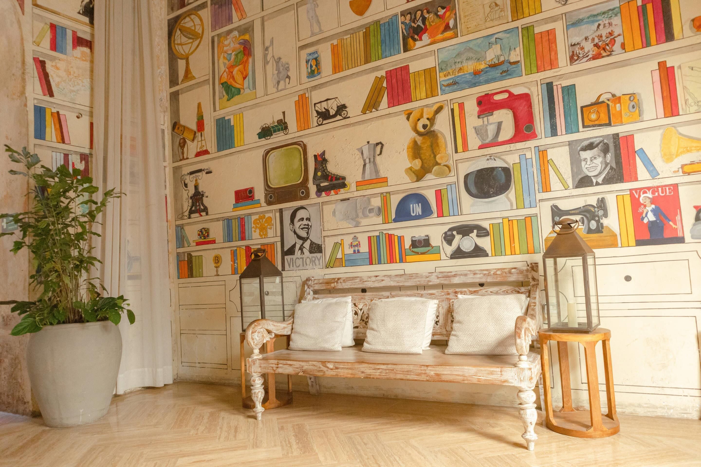Quarto com um banco de madeira, uma planta em vaso e uma parede decorada com diversos objetos.
