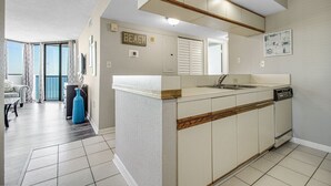 A modern kitchen with a central island, a dining area with a sofa, and a view of the beach.