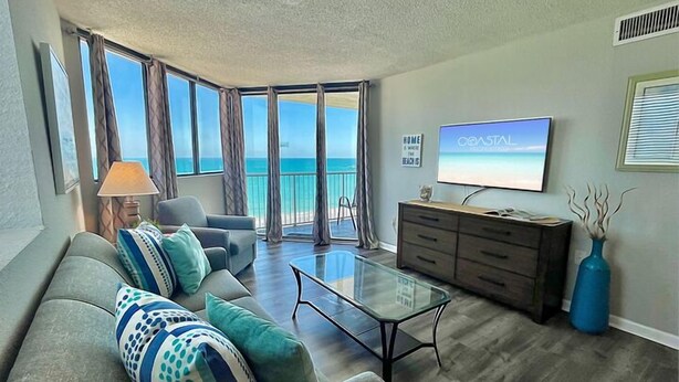 A living room with a sofa, a coffee table, a TV, and a view of the ocean.