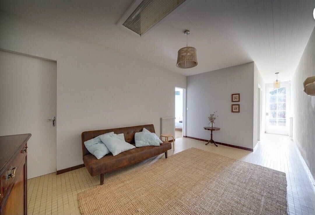 A spacious room with a large woven rug, a brown sofa with cushions, a wooden cabinet, and a hanging light fixture.