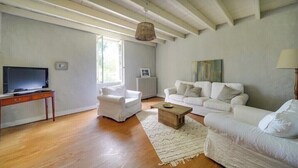 Un salón amplio con suelo de madera, sofás blancos, una mesa de centro y un televisor sobre un mueble de madera.