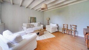 Un salón amplio con muebles blancos, una mesa de centro de madera y una lámpara colgante.