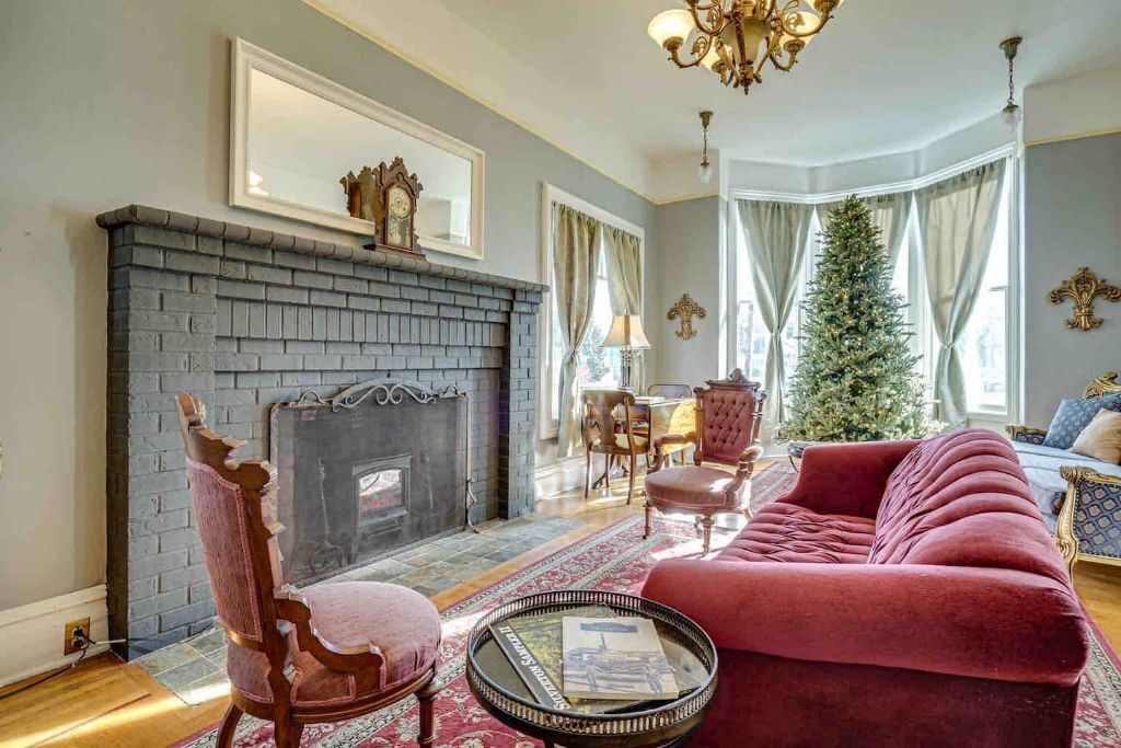 A living room with a fireplace, a red sofa, a wooden chair, and a Christmas tree.
