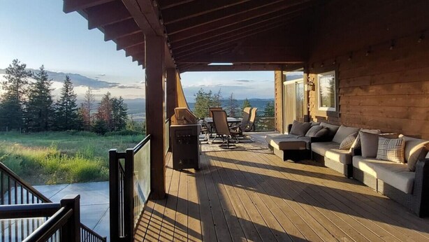 Eine Holzterrasse mit Gartenmöbeln, einem Grill und Blick auf Berge.