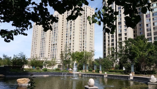 Un edificio residencial de gran altura con un jardín ajardinado que incluye un estanque, fuentes y esculturas de piedra.
