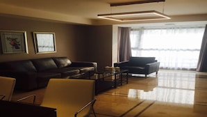 Una sala de estar moderna con un sofá de cuero, un sillón amarillo, una mesa de centro de vidrio y un ventanal con cortinas.