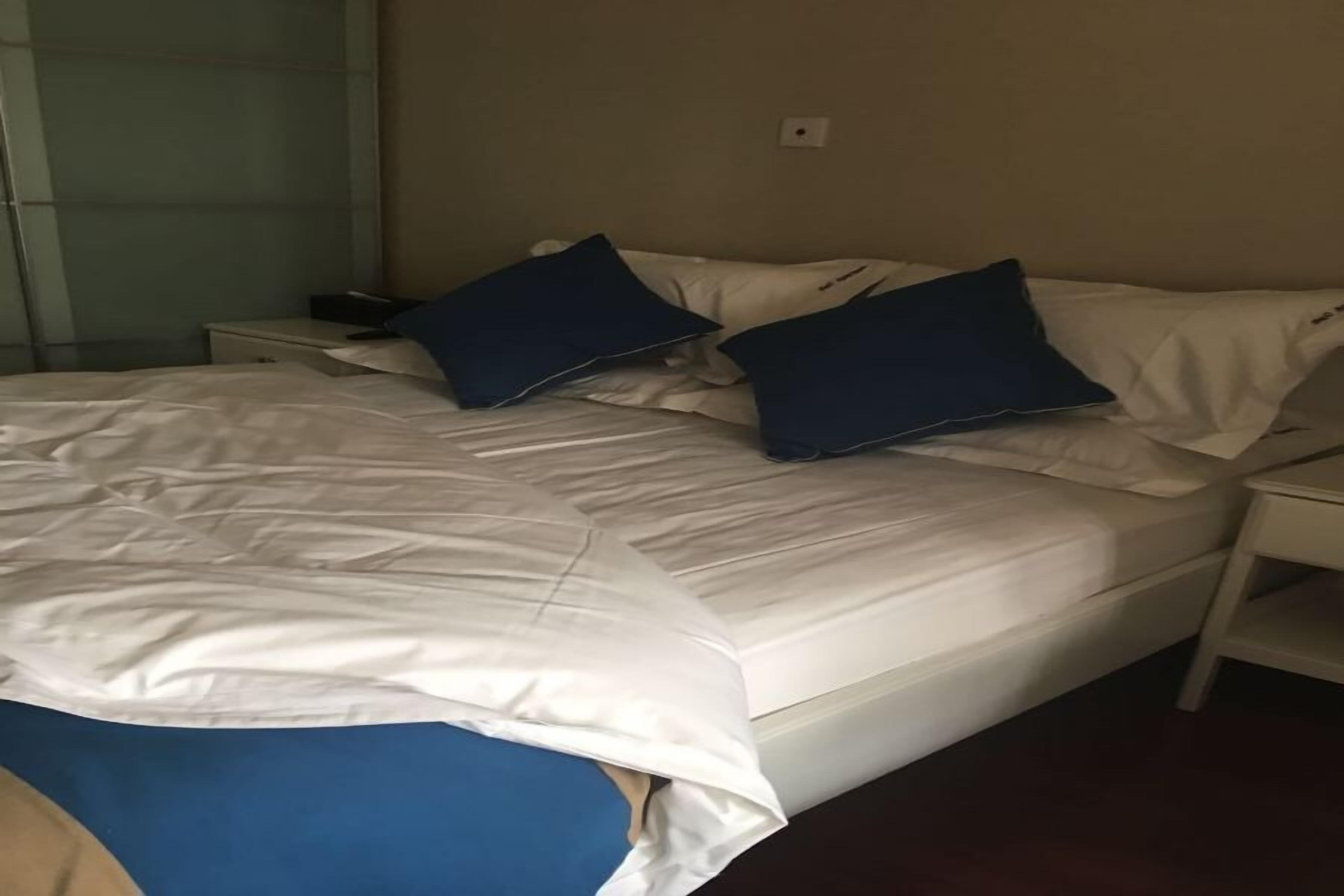 A bed with white bedding and two blue pillows, a bedside table, and a nightstand.