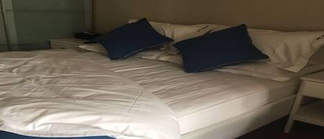 A bed with white bedding and two blue pillows, a bedside table, and a nightstand.