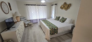 A bedroom with a bed, a TV, a desk, a chair, and a lamp.