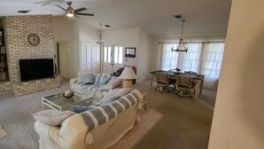 A living room with a brick fireplace, a sofa, a coffee table, and a dining area with a table and chairs. - Spacious South Venice Home (Venice)