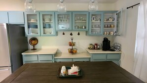 A kitchen with light blue cabinets, a stainless steel refrigerator, and a dining table with a tray of food. - Spacious South Venice Home (Venice)
