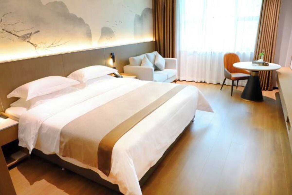 A hotel room with a large bed, a sofa, a small table, and a wall with artwork.
