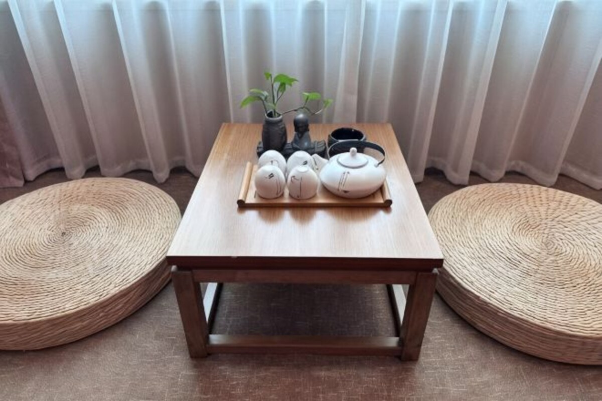 A wooden table with a tray of teapots and a plant, surrounded by woven mats.