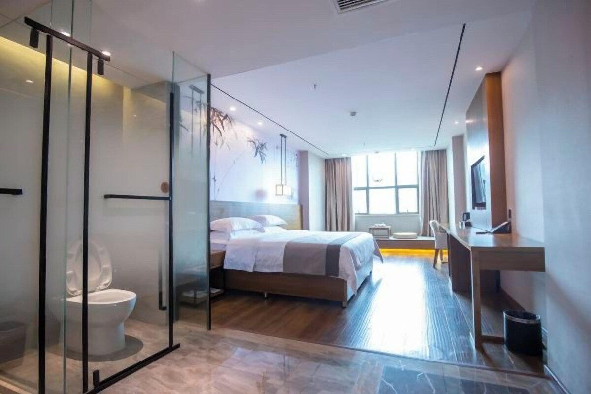A modern hotel room with a glass-enclosed shower, a large bed, a desk, and a TV.