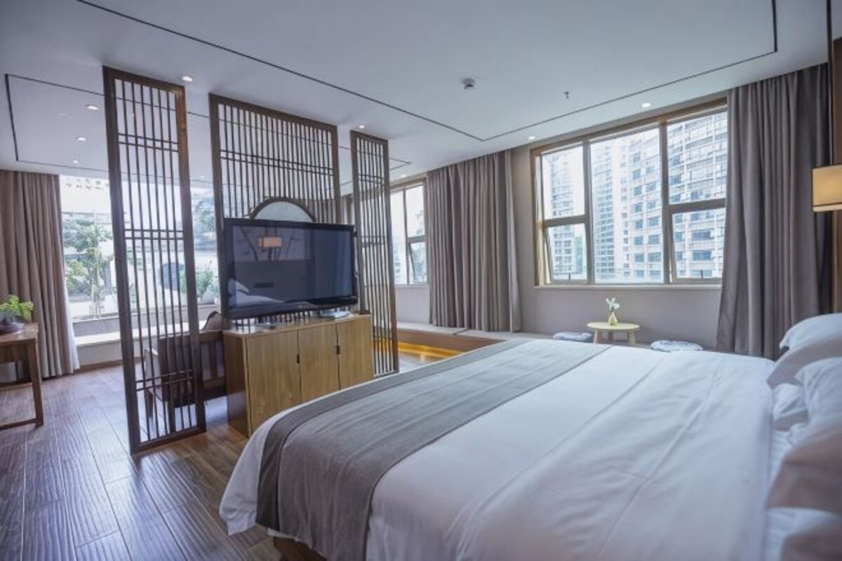 A hotel room with a bed, a TV, a small table, and a window with a view of buildings.