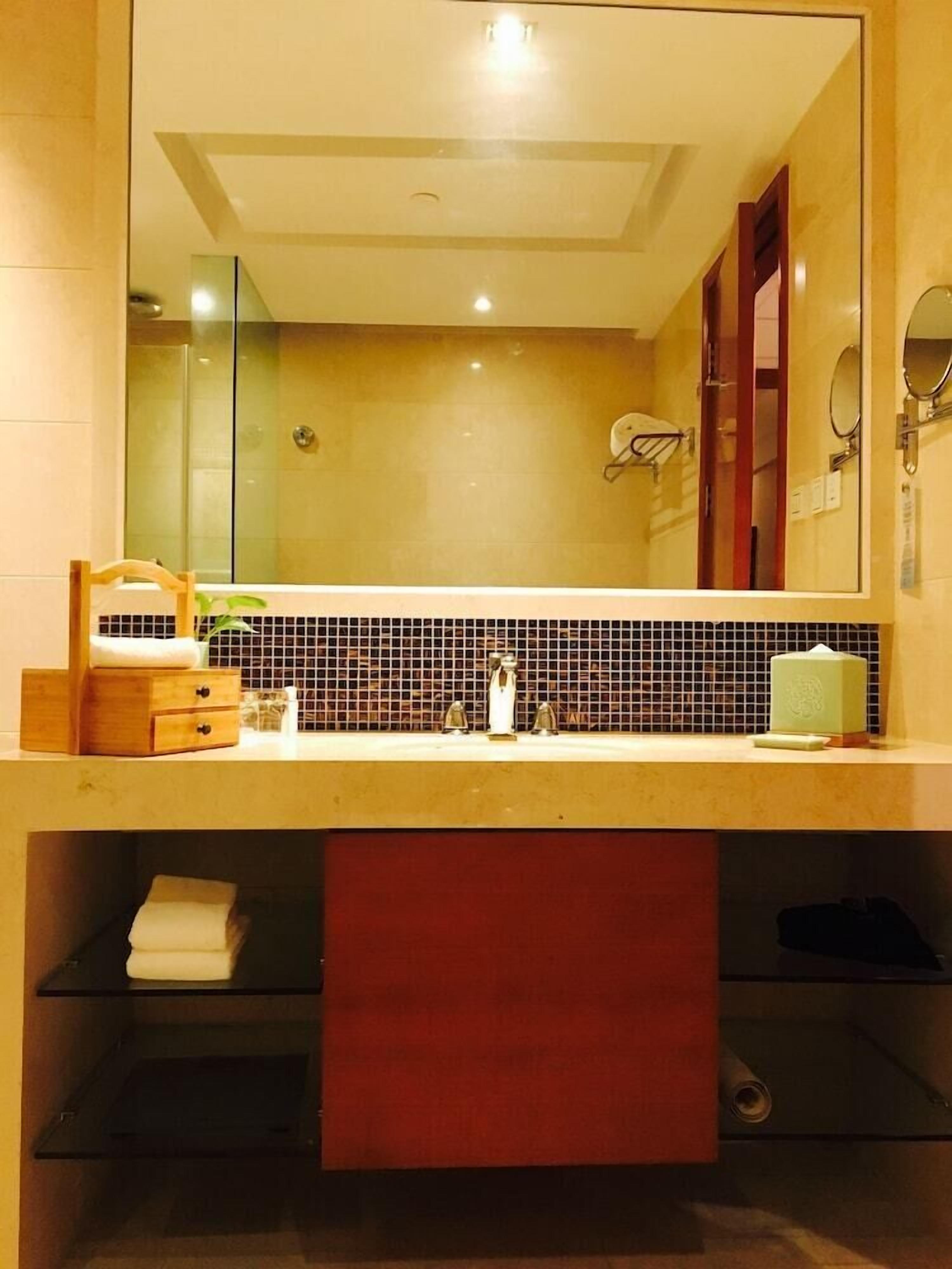 Een badkamer met een grote spiegel, een wastafel met handdoekhouder en een betegelde spatwand.