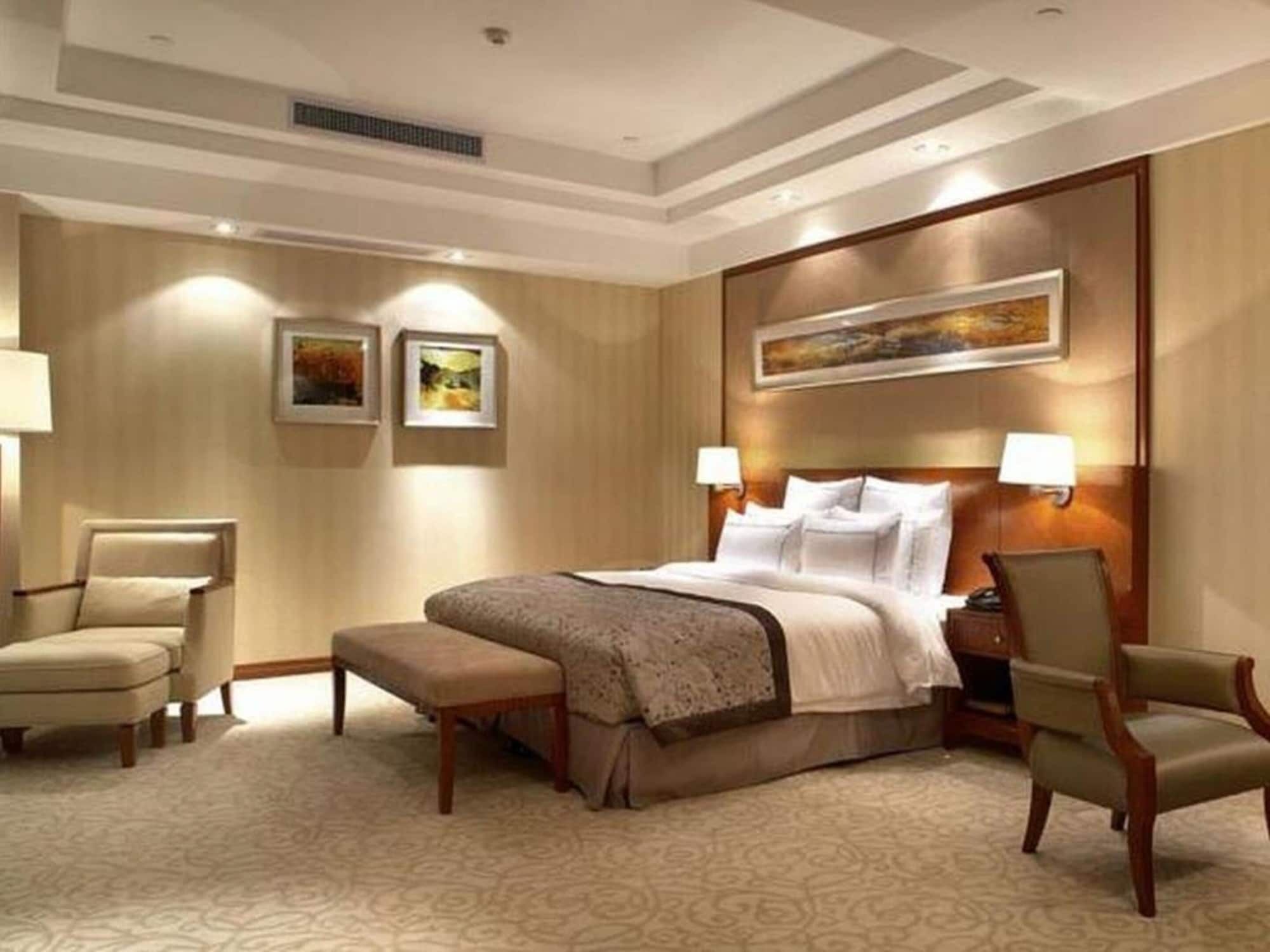 A hotel room with a large bed, two armchairs, a bench, and a headboard with a painting.