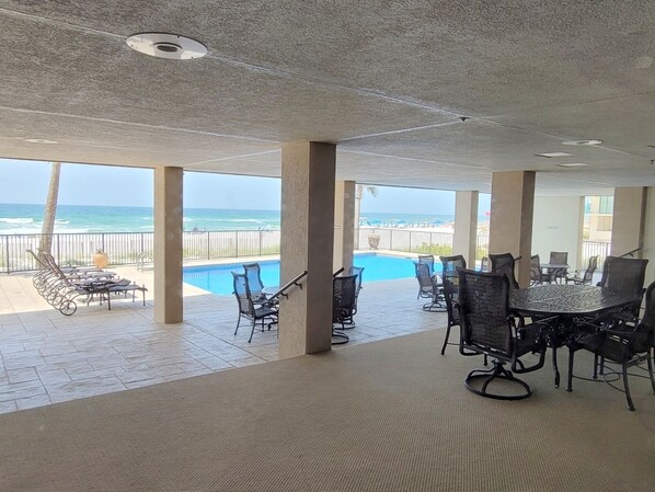 Un espace extérieur aménagé avec une piscine, des chaises et des tables, offrant une vue sur l’océan.