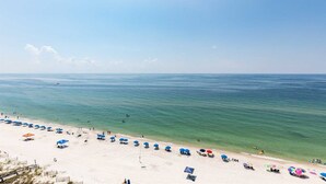 Ein Strand mit Reihen von Sonnenschirmen und Liegestühlen, einem klaren Himmel und ruhiger See.