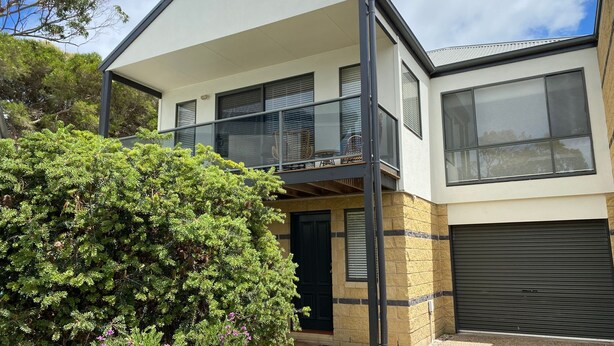 A two-story house with a balcony, a garage, and a large bush in the foreground. - Perfect Location - Inverloch (INVERLOCH)