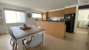 A modern kitchen with wooden cabinets, a central island, and a dining area with white chairs. - Perfect Location - Inverloch (INVERLOCH)