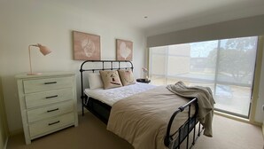 A bedroom with a bed, a nightstand, a dresser, and a window with a view of the outside. - Perfect Location - Inverloch (INVERLOCH)