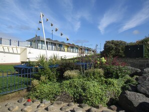 Et kysthotel med flere balkoner, en have med forskellige planter og en klar blå himmel.