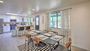 Una cocina moderna con armarios blancos, un microondas y un refrigerador. Hay un comedor con una mesa dispuesta para seis personas, sillas y un tapete a rayas.