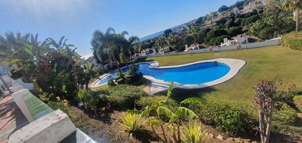 Piscina rodeada de exuberante vegetación y vistas a un pueblo costero.