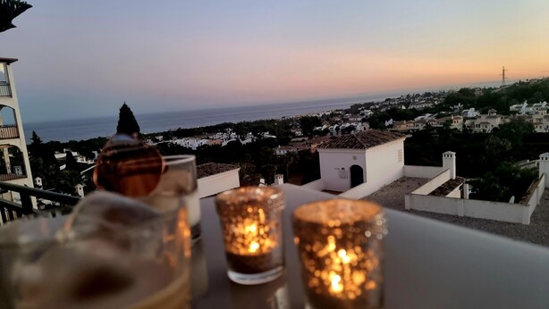 A table with three lit candles and a bowl, overlooking a coastal town at sunset. - Relax your mind (Mijas)