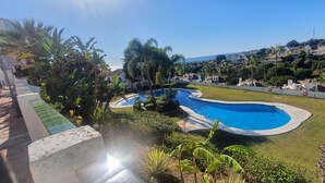 A swimming pool surrounded by lush greenery and palm trees, with a view of a coastal town in the background. - Relax your mind (Mijas)